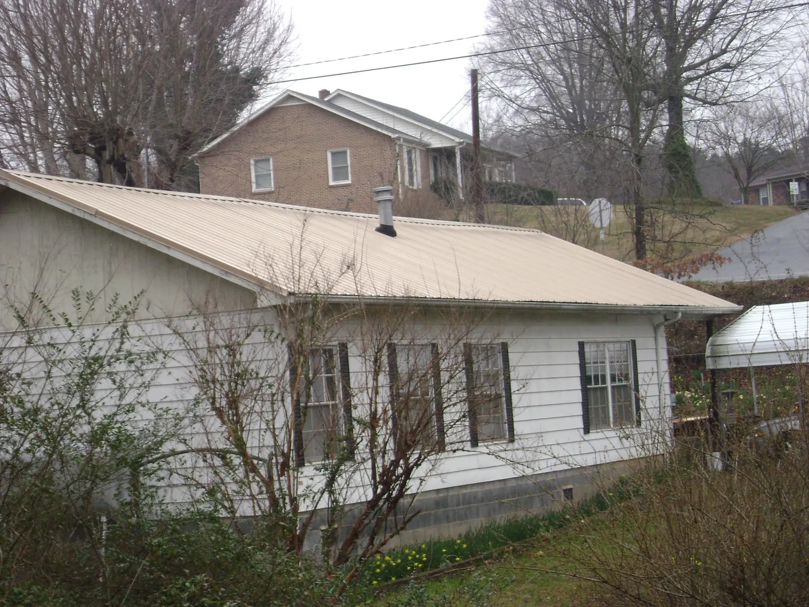 Tan metal roof on a white sided house set into a hillside — Commercial Roofing by Roofing Brothers in Stirling City